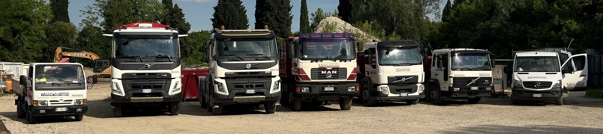 Il parco mezzi Tonini Srl: camion Volvo, MAN e Mercedes ed escavatore schierati nel piazzale